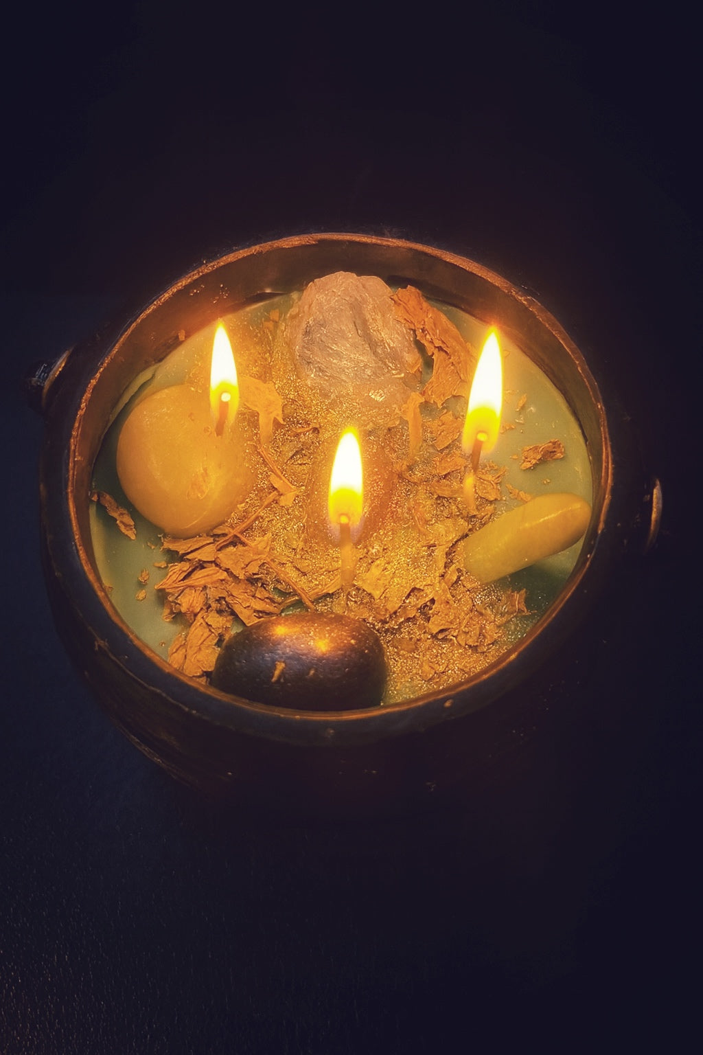 Ritual prosperity candle in a cast iron cauldron with crystals and herbs, crafted for Fortuna and wealth manifestation.